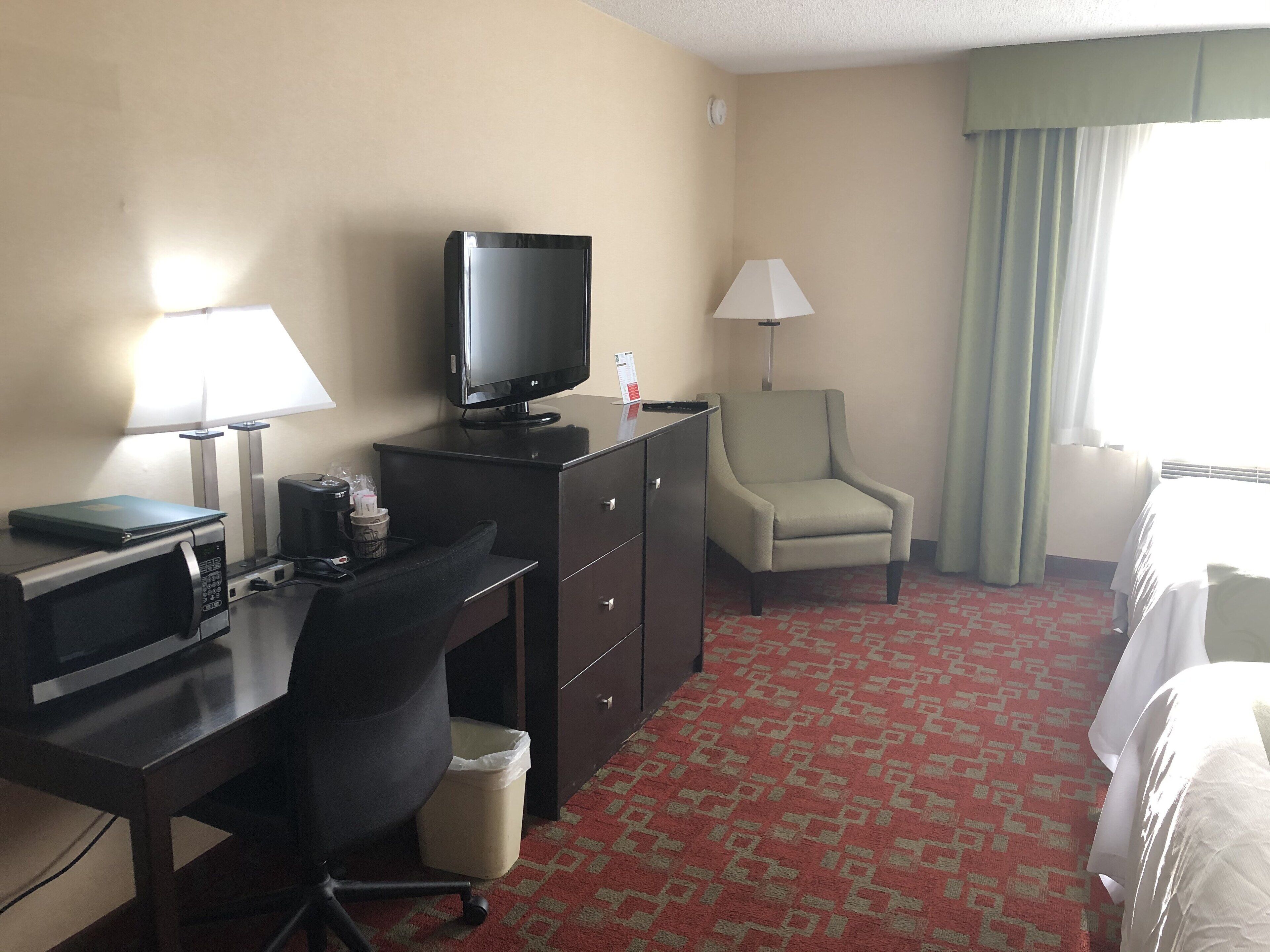 Une chambre d’hôtel équipée d’un bureau, d’une télévision, d’une chaise, d’une lampe et d’un lit.