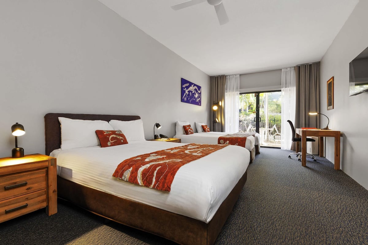 Ein Hotelzimmer mit einem großen Bett, einem Schreibtisch, einem Stuhl, einem Nachttisch, einer Lampe und einem Deckenventilator.
