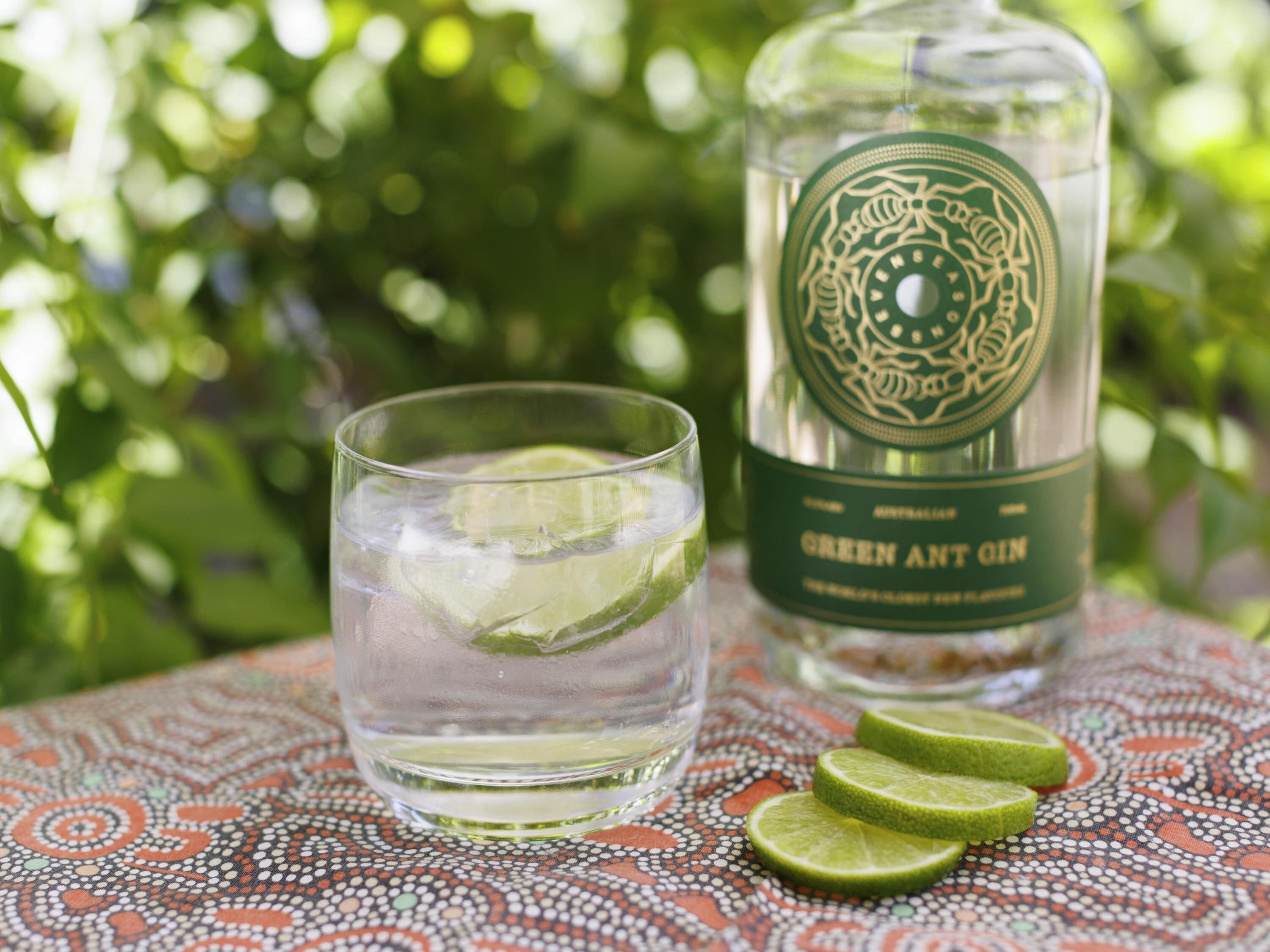 A glass of green ant wine with lime slices on a patterned tablecloth.