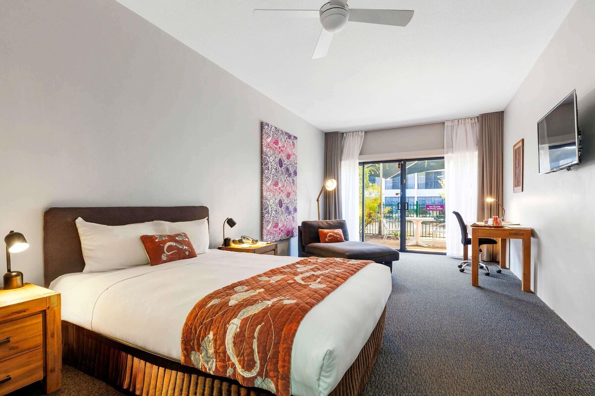 A hotel room with a bed, desk, chair, and a view of the outside.
