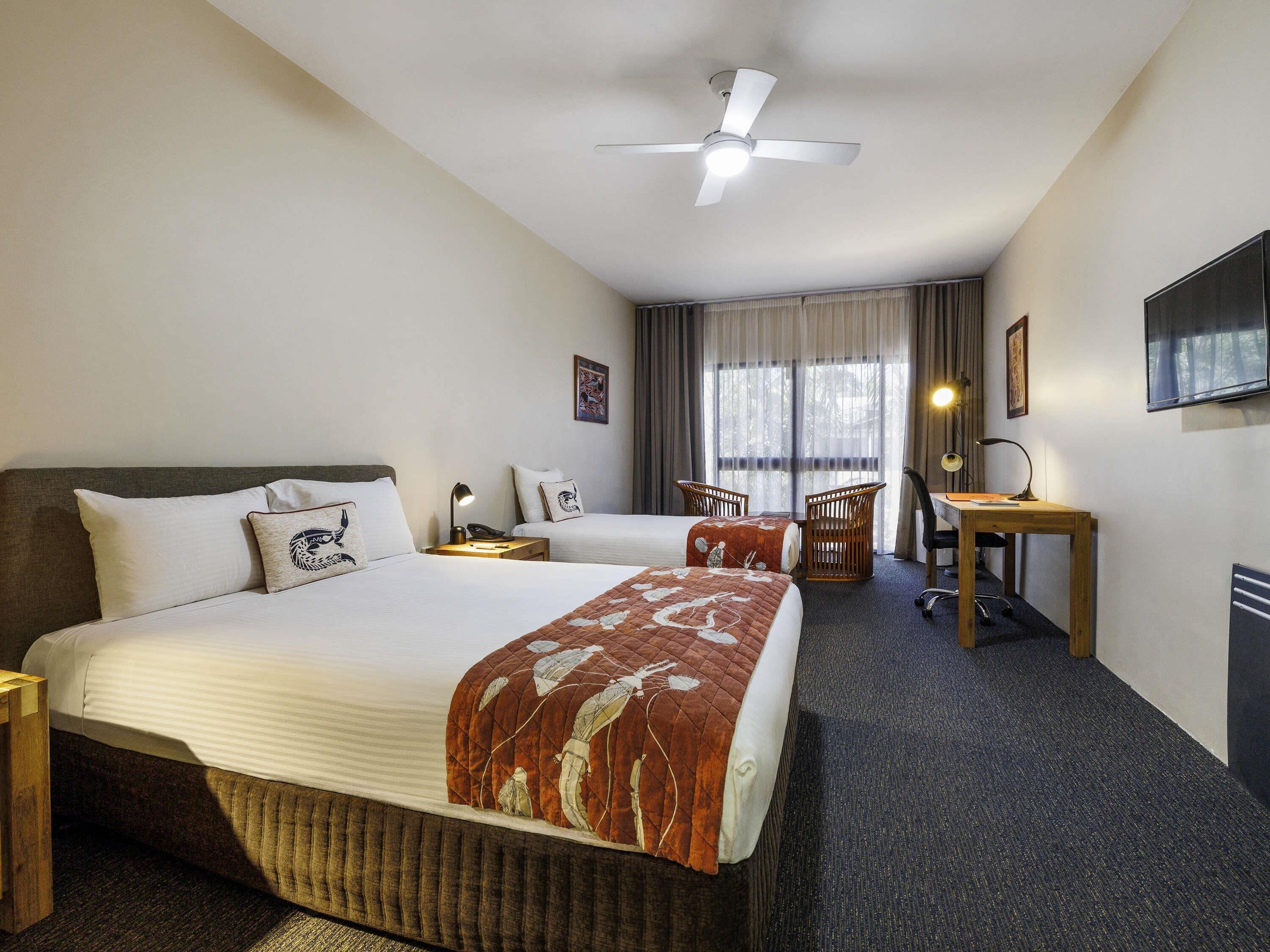 A hotel room with a large bed, a desk, a chair, a ceiling fan, and a window with curtains.