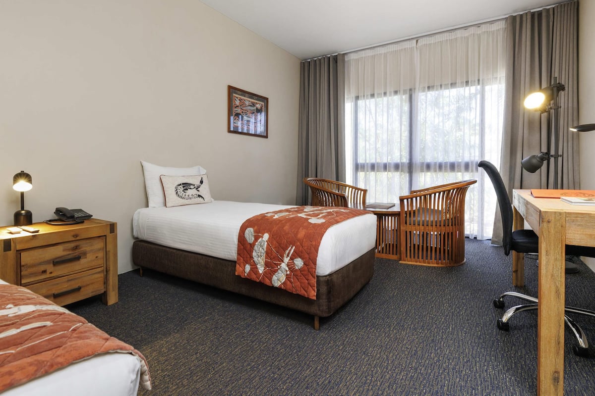 A hotel room with a bed, a desk, a chair, a nightstand, and a lamp.