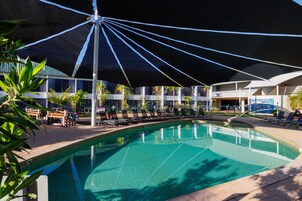 A swimming pool with lounge chairs and umbrellas, surrounded by a building with multiple levels and balconies.