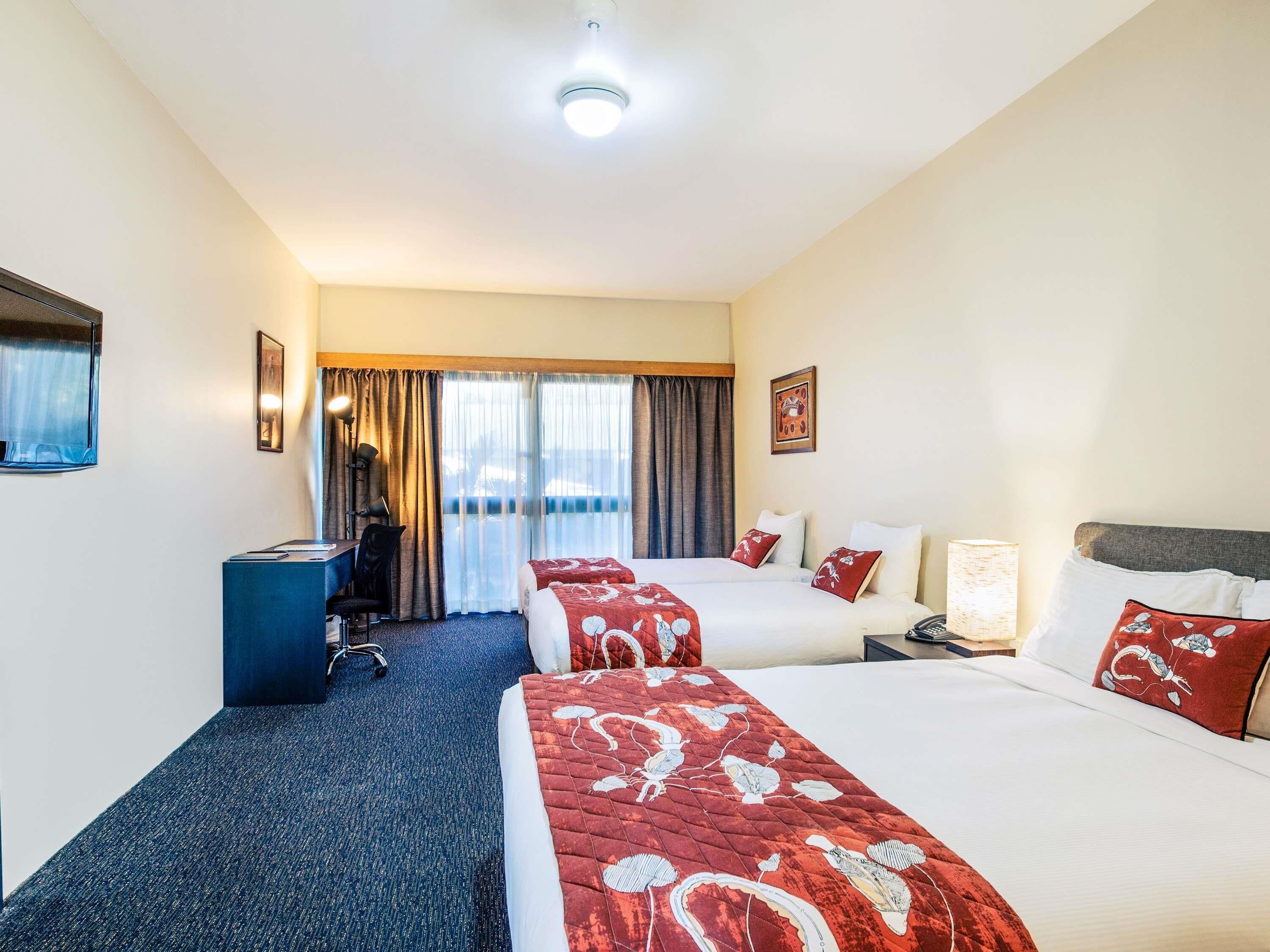 A hotel room with two beds, a desk, a chair, and a view of the outdoors.