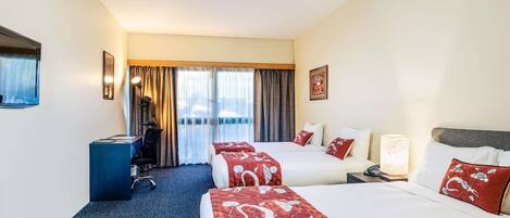 A hotel room with two beds, a desk, a chair, and a view of the outdoors.