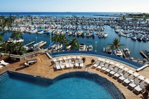 Un puerto deportivo con numerosas embarcaciones amarradas, un área de piscina con tumbonas y vistas al océano.