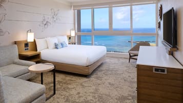 A hotel room with a bed, a sofa, a small table, a TV, and a view of the ocean.
