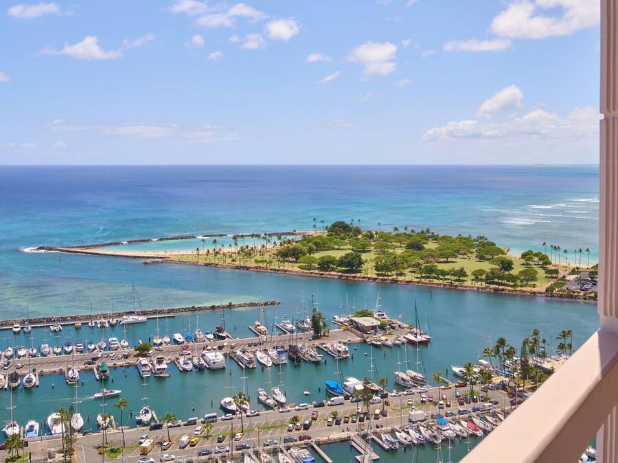 A marina with numerous boats docked, a clear blue sky, and a view of the ocean.