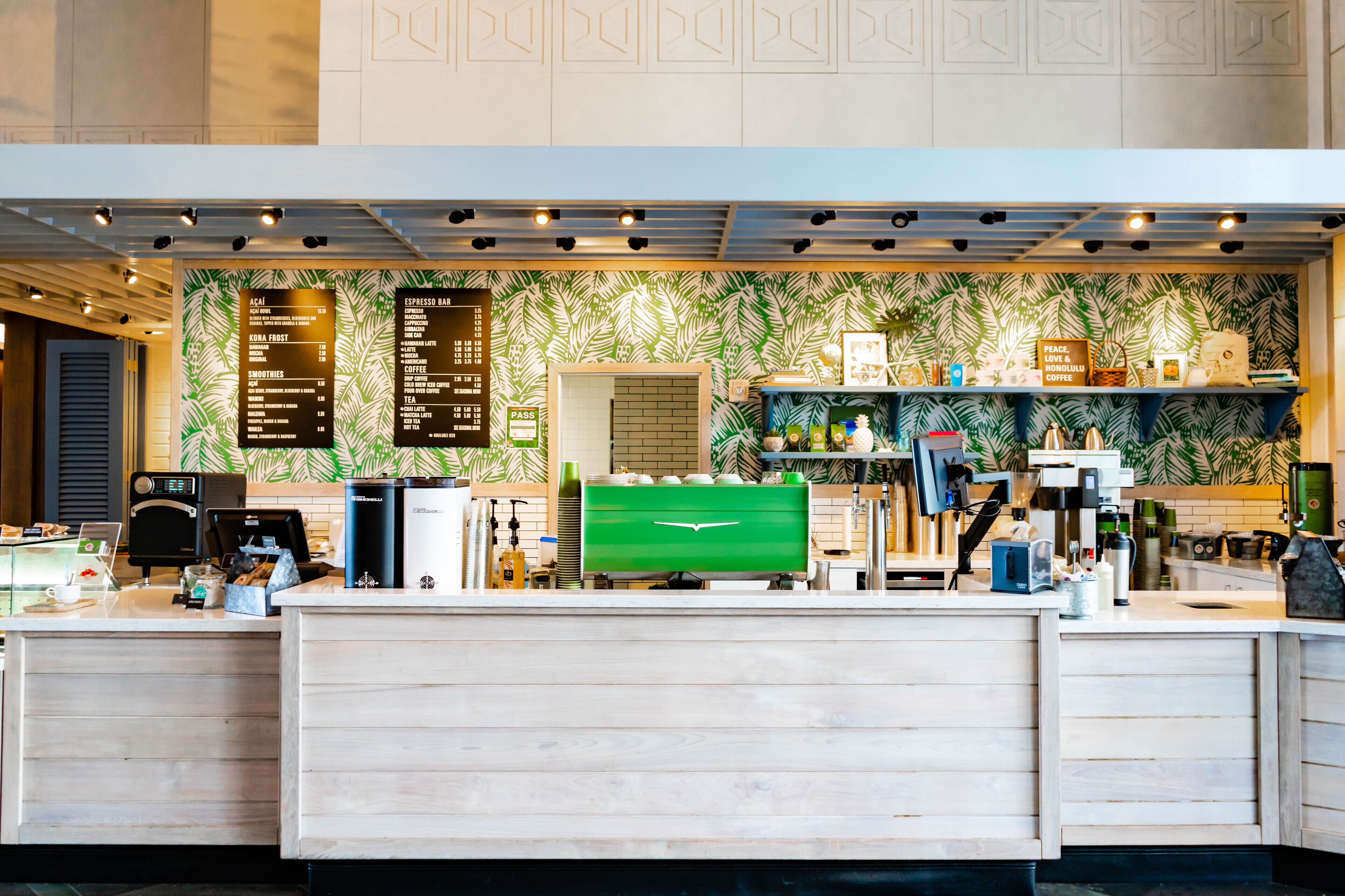 Een toonbank in een koffiezaak met een menubord, een espressoapparaat en een groene koffiemolen.