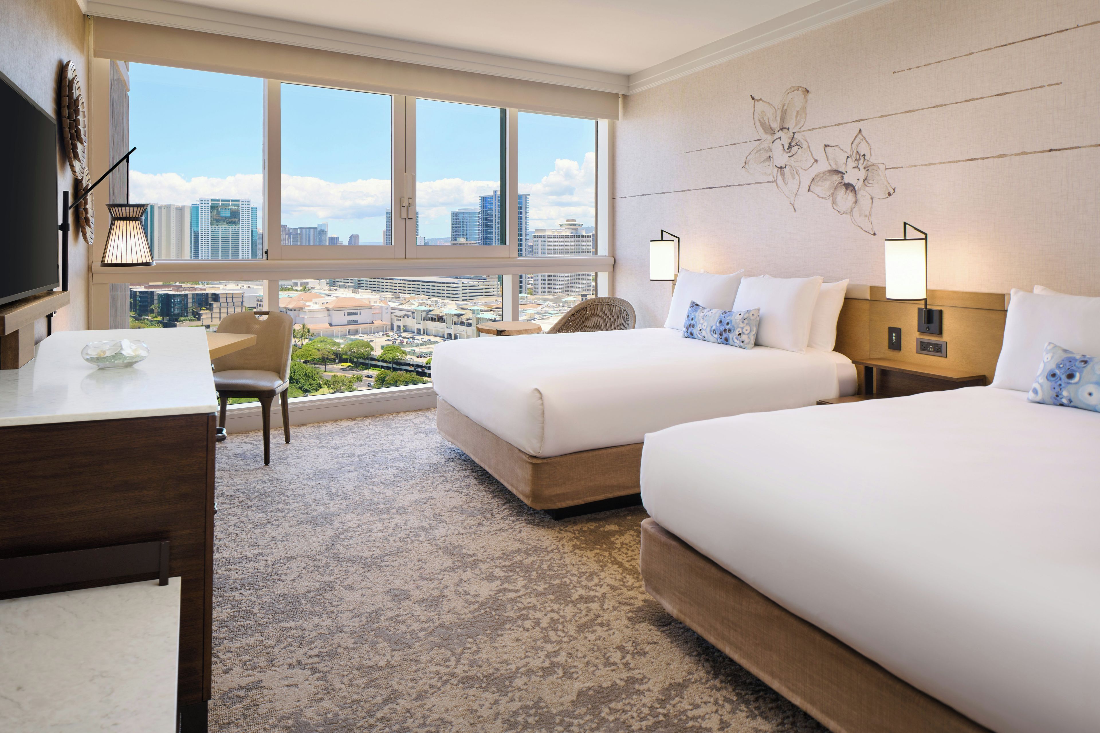 A hotel room with two beds, a desk, a chair, and a large window offering a city view.