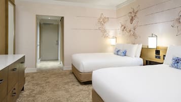 Habitación de hotel con dos camas, un aparador, una puerta que da a un pasillo y decoración en la pared.