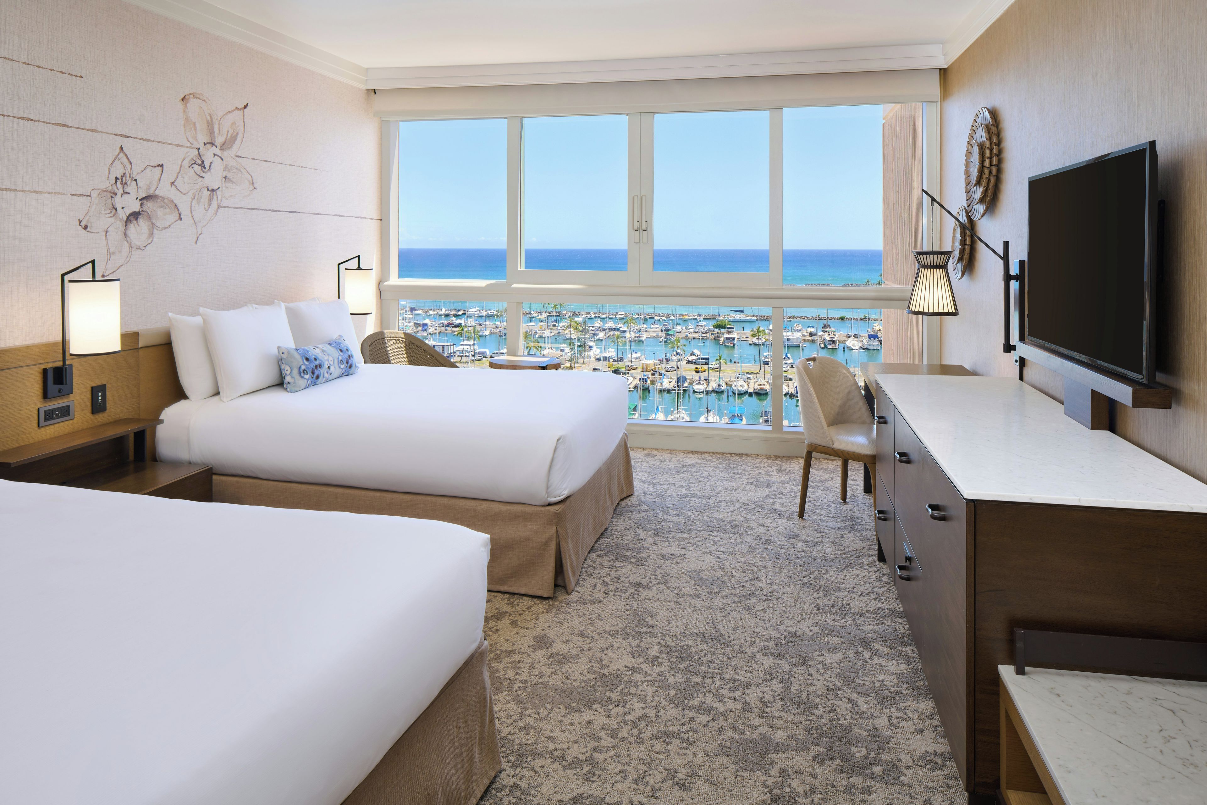 Habitación de hotel con dos camas, un escritorio, un televisor y vistas al puerto deportivo.