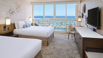 Habitación de hotel con dos camas, un escritorio, un televisor y vistas al puerto deportivo.