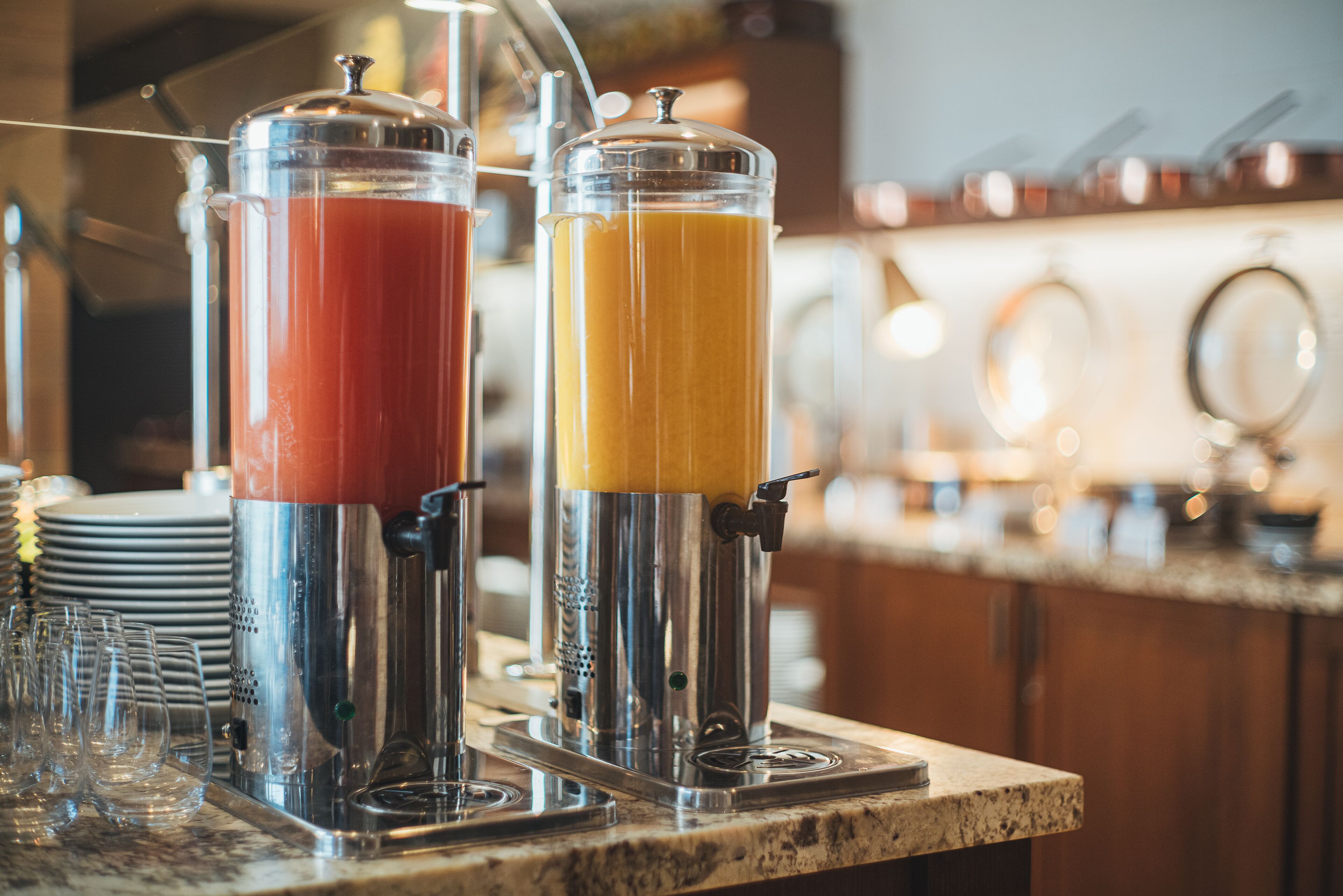 Un distributeur de jus avec deux liquides de couleurs différentes, une pile d’assiettes et un comptoir de bar.
