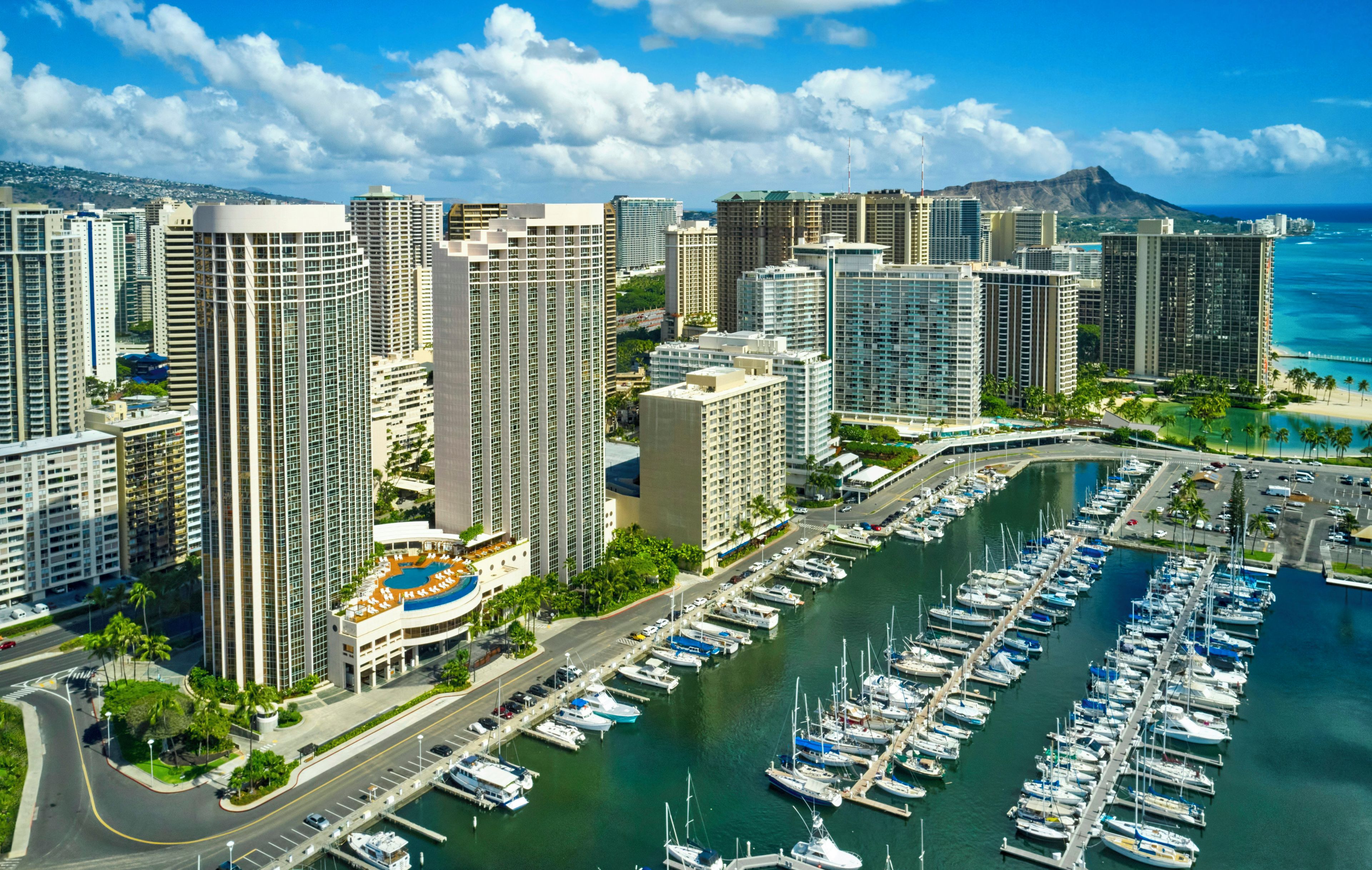 A marina with numerous boats docked, surrounded by high-rise buildings and a clear sky.