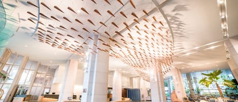 Een ruime lobby met een hoge plafond, moderne zithoeken en een receptiebalie.
