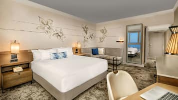 Habitación de hotel con una cama grande, un escritorio con una computadora portátil, un sofá y un espejo que refleja un balcón.