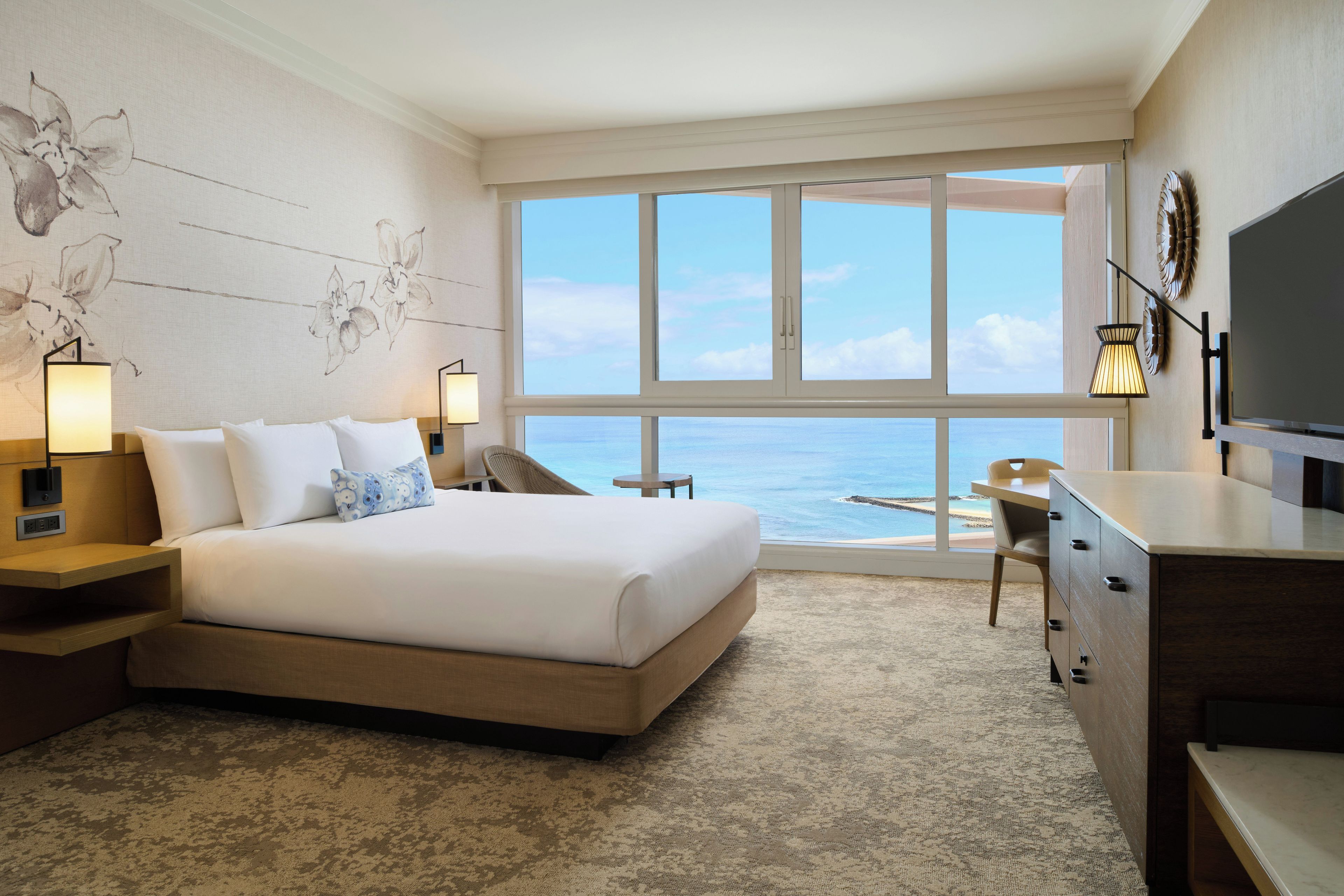 Een hotelkamer met een groot bed, een bureau, een stoel, een televisie en uitzicht op de oceaan.