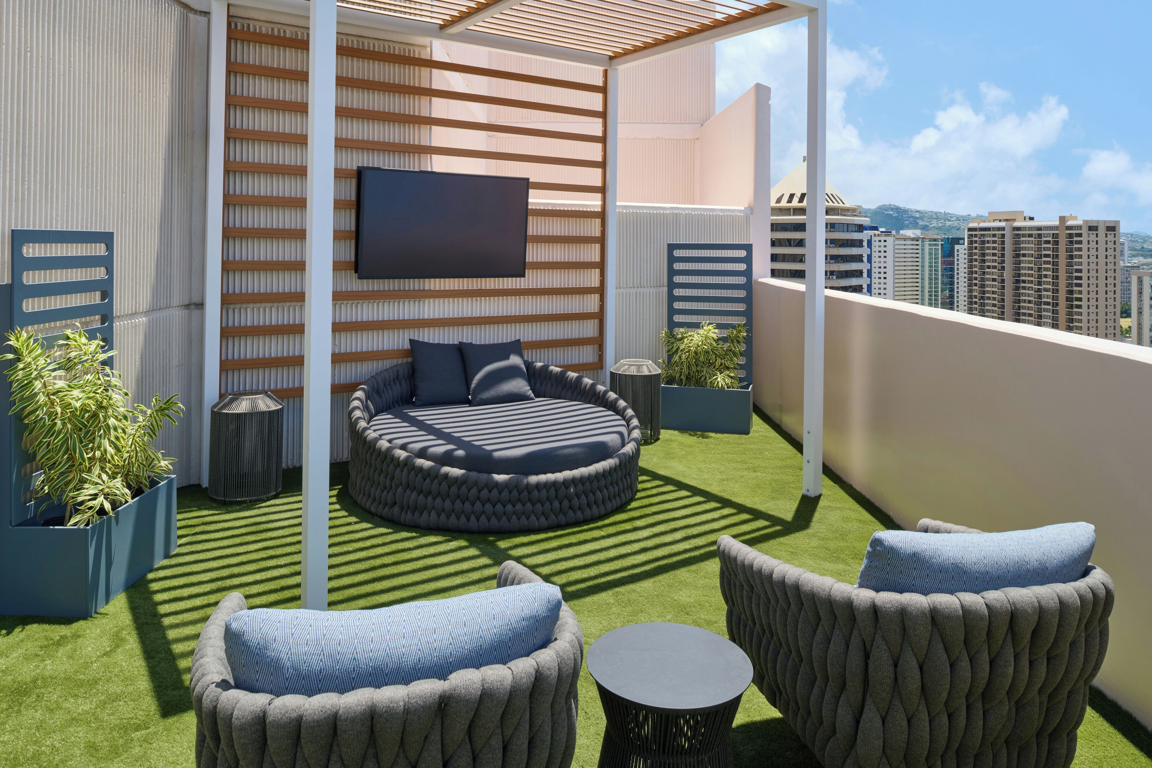 Una terraza en la azotea con un área de estar circular, dos sillones, una mesita, un televisor de pantalla plana y plantas en macetas.