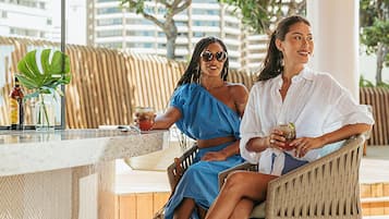 Two people seated at an outdoor bar with a view of buildings and trees.