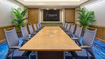 A conference room with a long table, multiple chairs, and a screen displaying "PRINCE WAIKI".