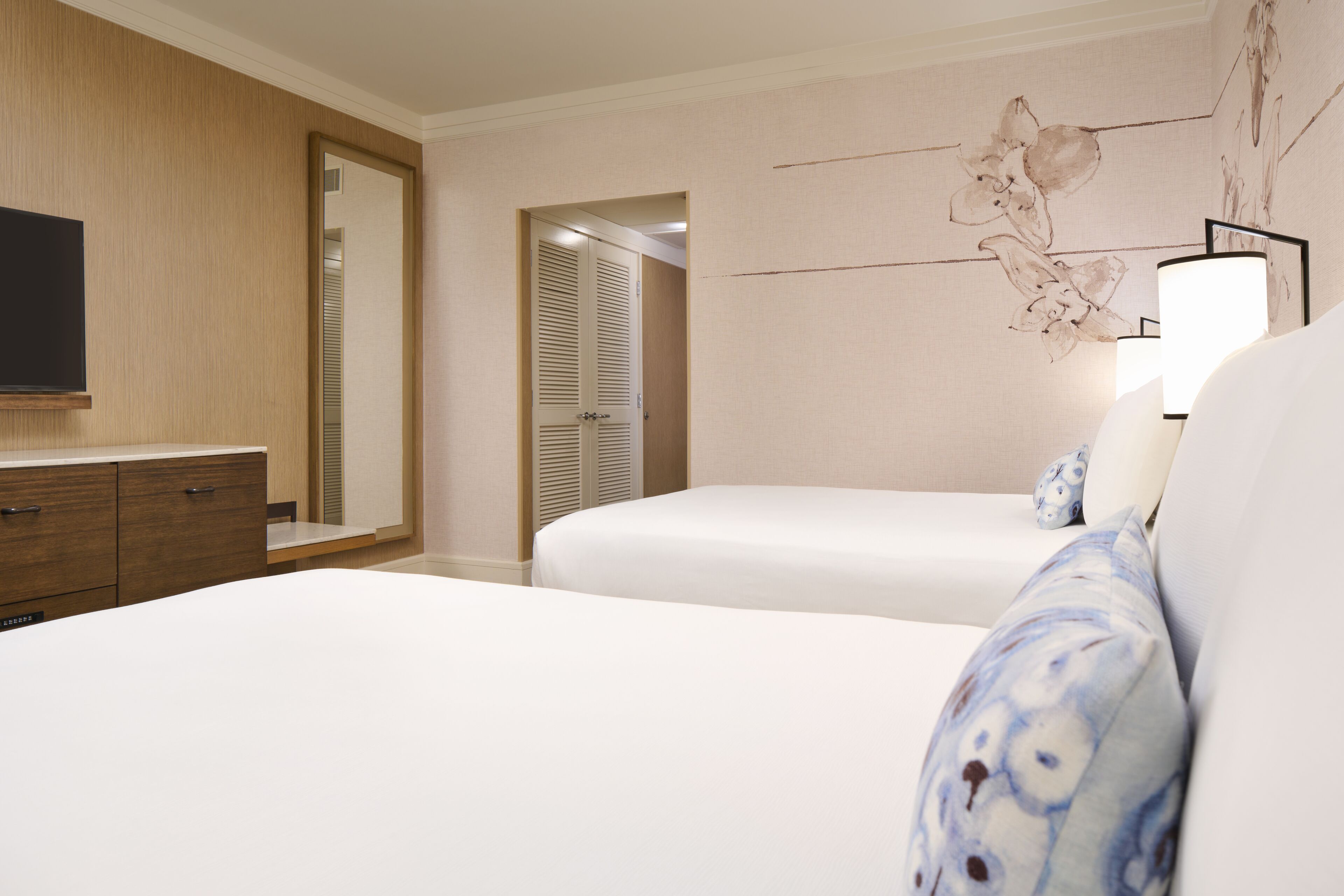 Une chambre d’hôtel avec une armoire en bois, un téléviseur à écran plat, un lit avec du linge de lit blanc et une lampe fixée au mur.