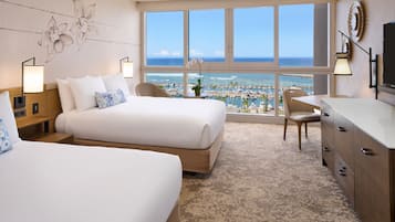 Habitación de hotel con dos camas, un escritorio, una silla, un televisor y un ventanal grande con vistas a la playa y el puerto deportivo.