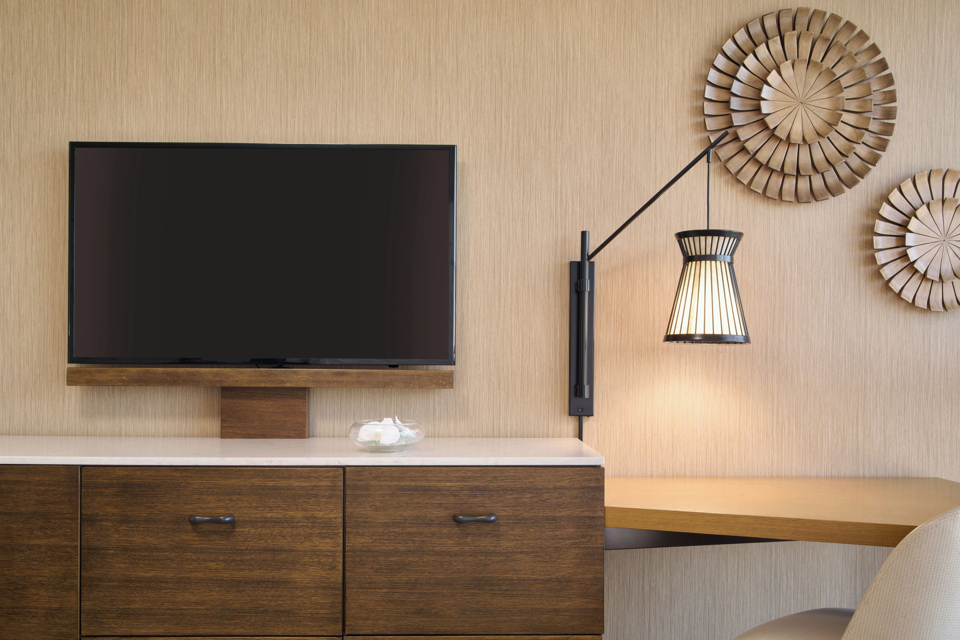 Una sala de estar moderna con un televisor de pantalla plana montado en una pared de madera, una mesa de centro de vidrio y un mueble de madera con cajones.