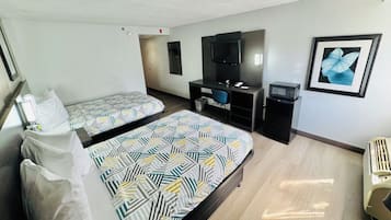 A hotel room with two beds, a desk, a TV, a framed picture, and a radiator.