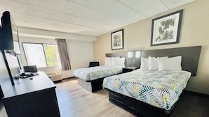 A hotel room with two beds, a desk, a chair, a window with curtains, and framed artwork on the walls.