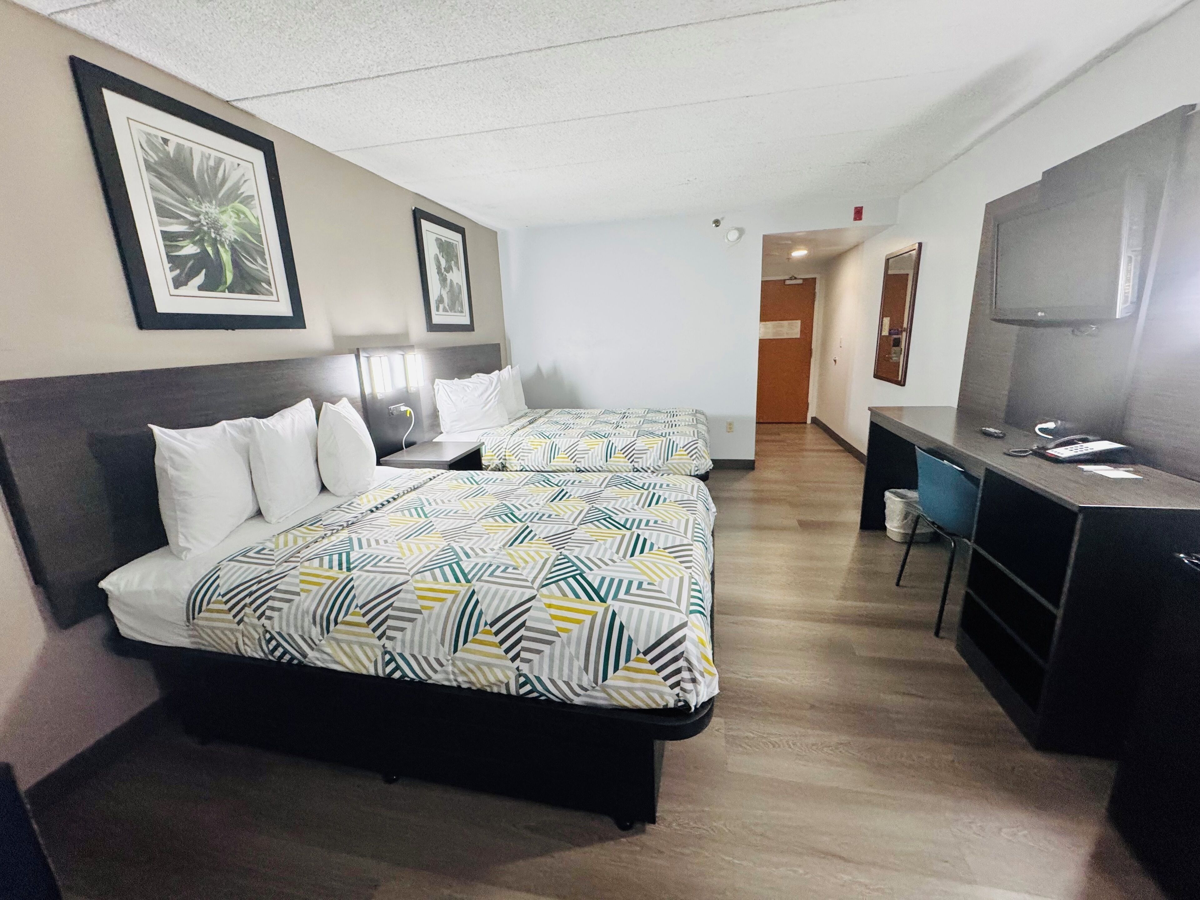 A hotel room with two beds, a desk, a chair, and a television.