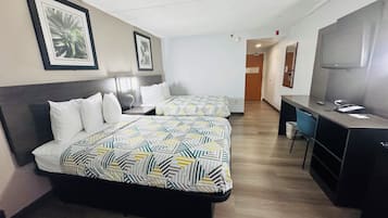 A hotel room with two beds, a desk, a chair, and a television.