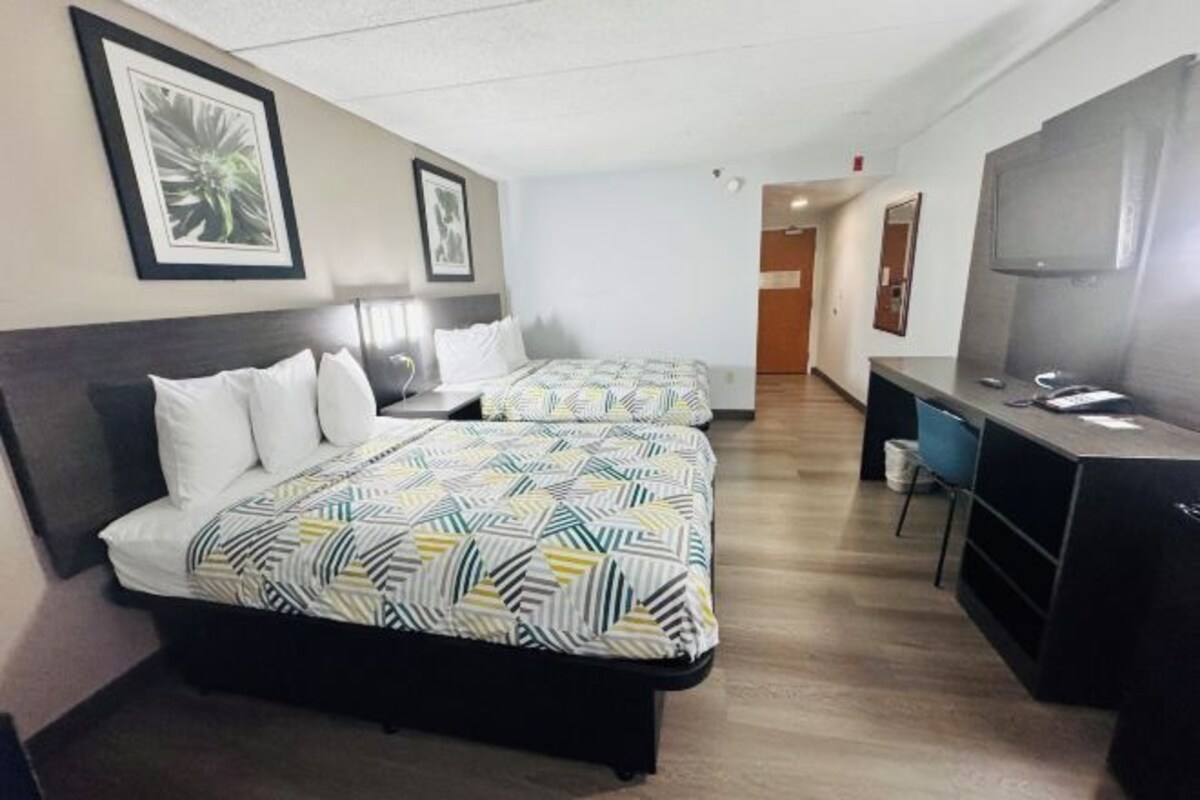 A hotel room with two beds, a desk, a chair, and a television.