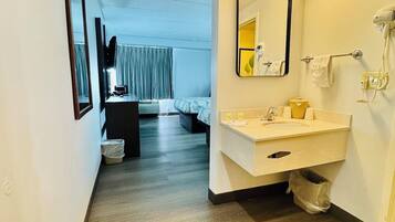 A hotel room with a wooden floor, a white sink, a mirror, and a bed with a blue and white patterned bedspread.