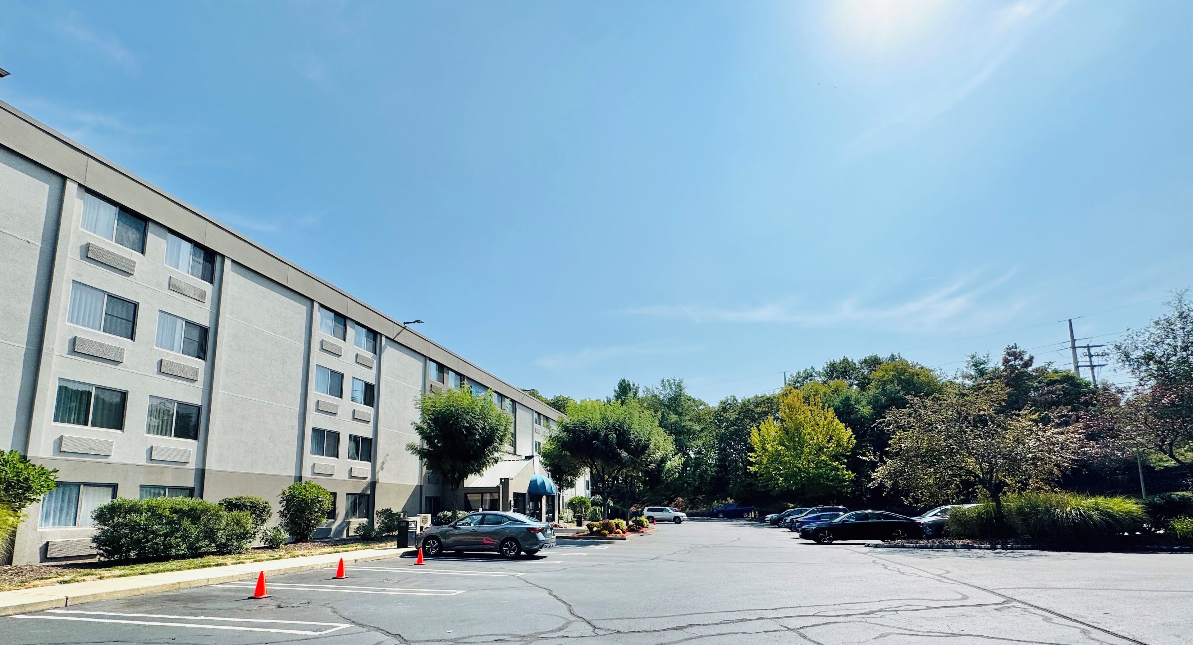 A parking lot with several cars, a building with multiple windows and air conditioning units, and trees with green and yellow foliage.