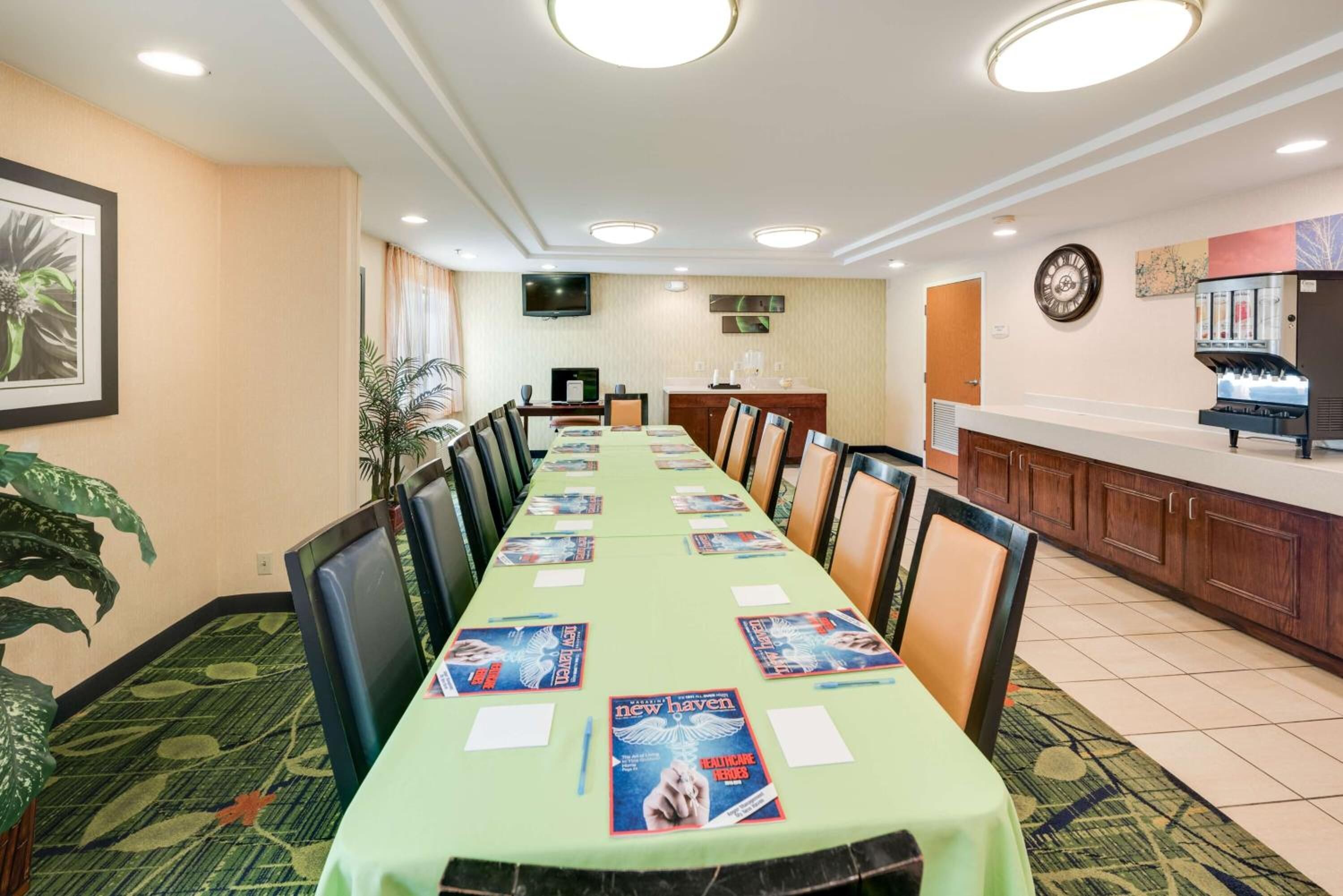 A conference room with a long table, chairs, a coffee machine, and a TV on the wall.