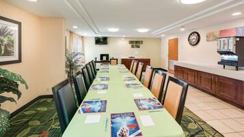 A conference room with a long table, chairs, a coffee machine, and a TV on the wall.