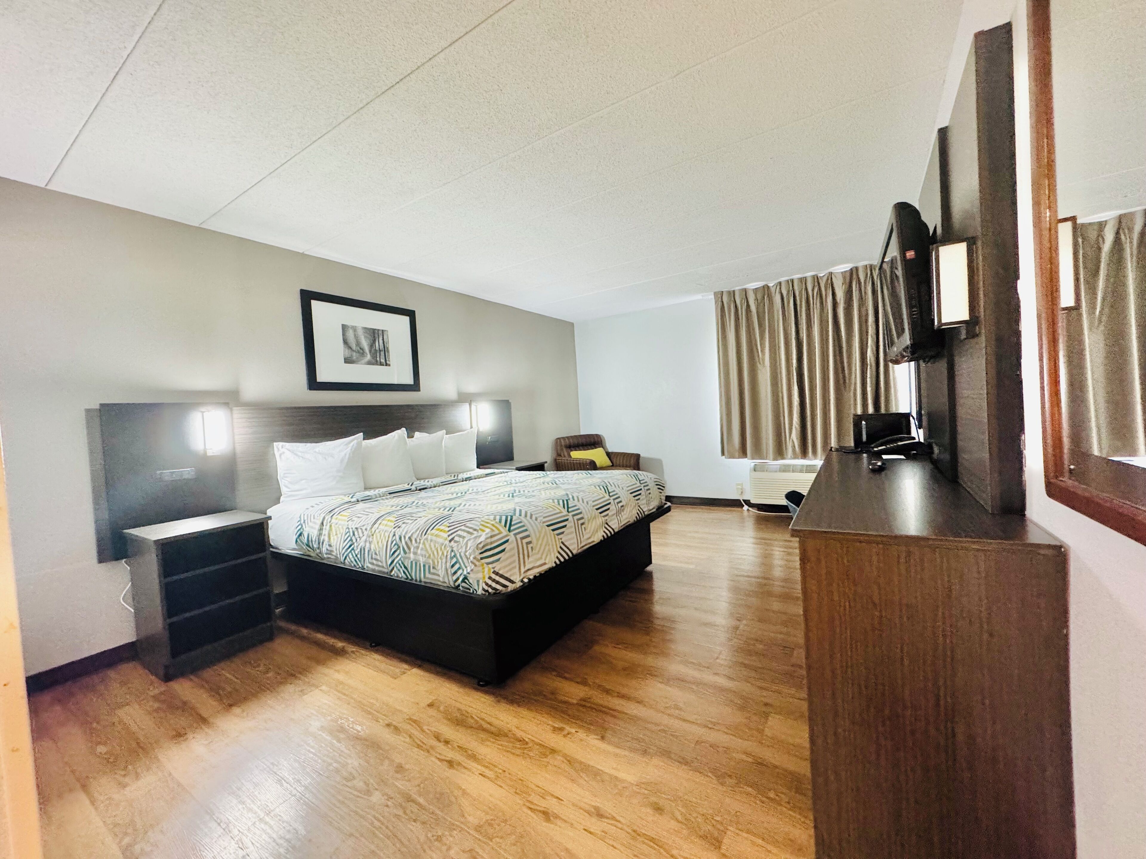 A hotel room with a bed, bedside tables, a desk, a chair, a television, and a window with curtains.