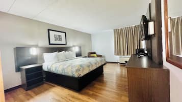 A hotel room with a bed, bedside tables, a desk, a chair, a television, and a window with curtains.