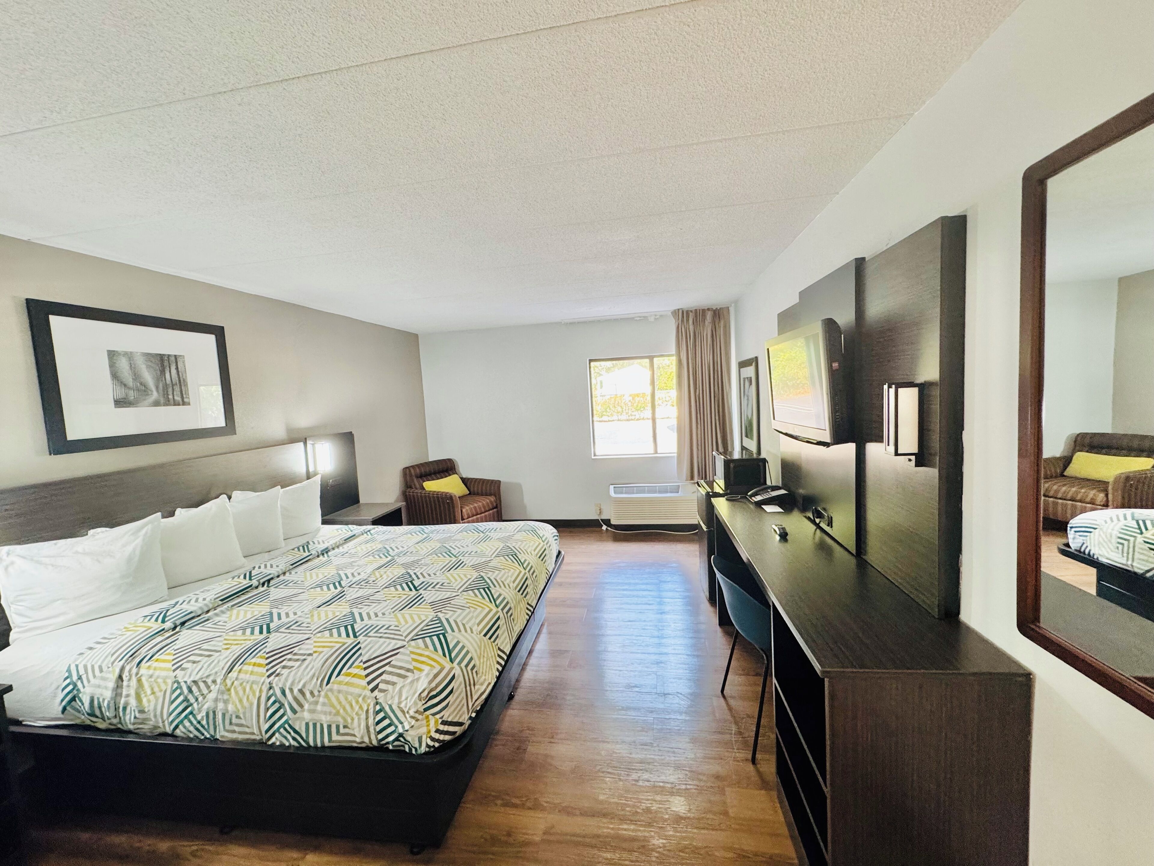 A hotel room with a large bed, a desk, a chair, a TV, and a window with curtains.