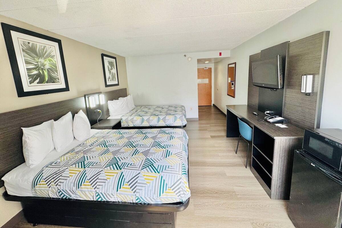 Ein Hotelzimmer mit zwei Betten, einem Schreibtisch, einem Fernseher und einem Spiegel.