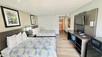 A hotel room with two beds, a desk, a TV, and a mirror.