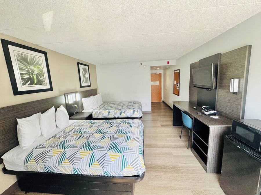 A hotel room with two beds, a desk, a TV, and a mirror.