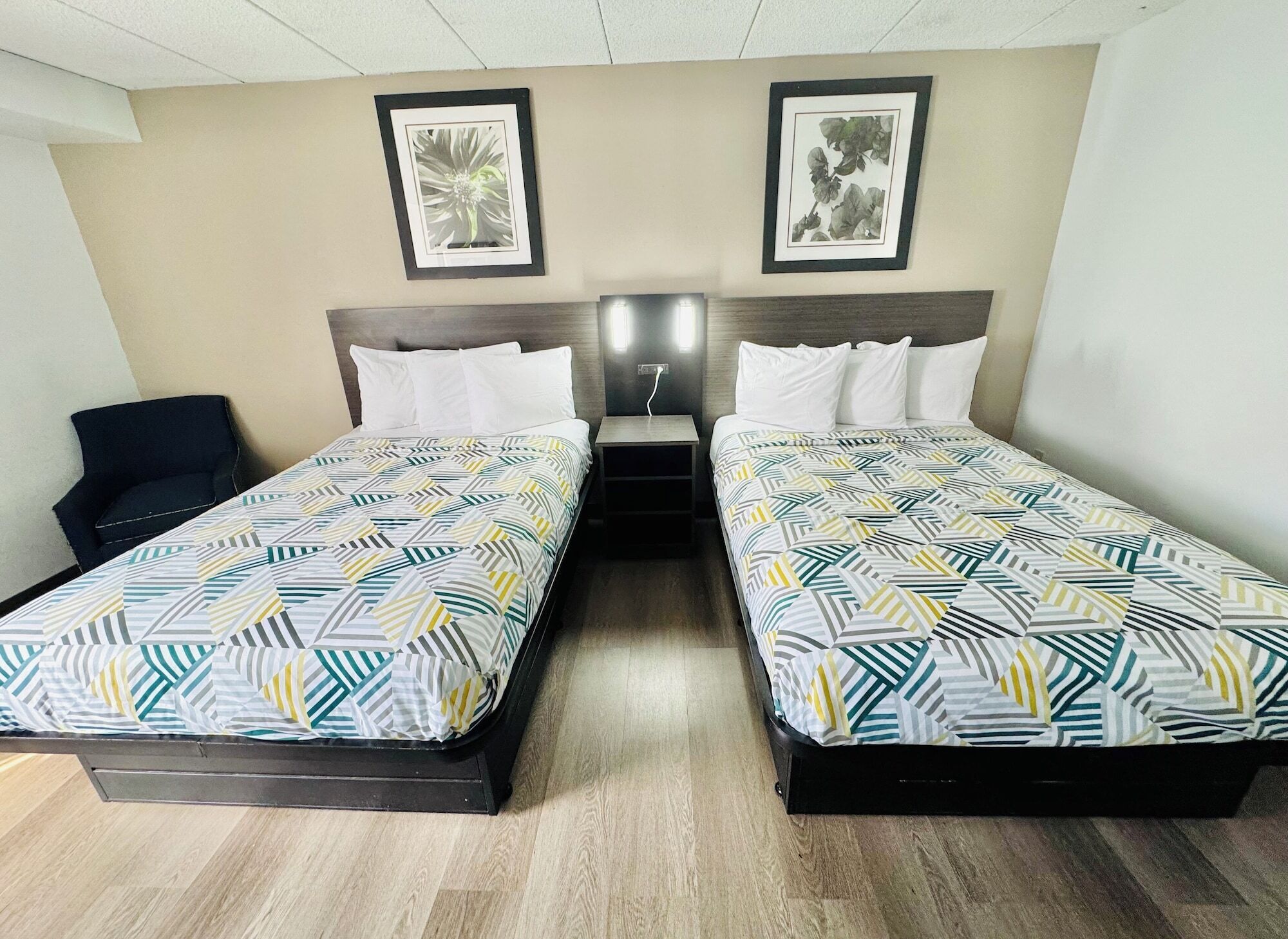 Une chambre d’hôtel avec deux lits, une table de chevet, une chaise et des œuvres d’art encadrées accrochées aux murs.
