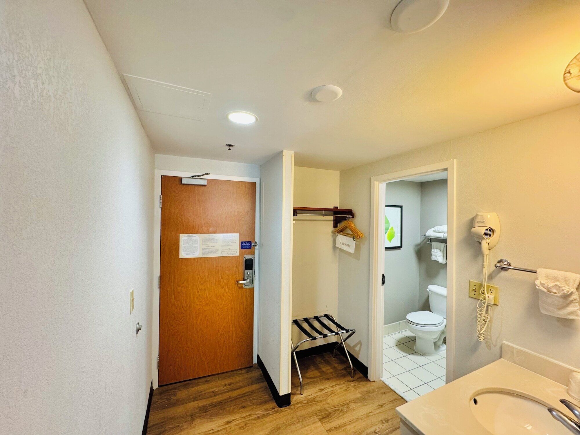 Ein Hotelbad mit Holzboden, Waschbecken, Toilette und einem an der Wand befestigten Föhn.