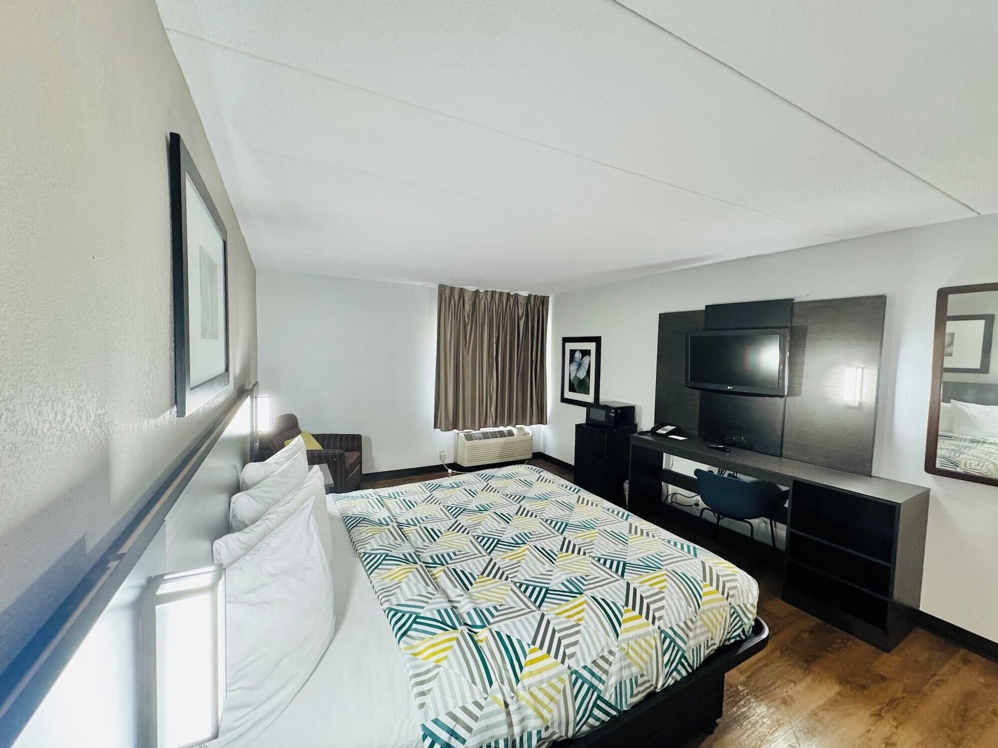 Una camera d'albergo con un letto, una scrivania con televisore, uno specchio e una finestra con tende.