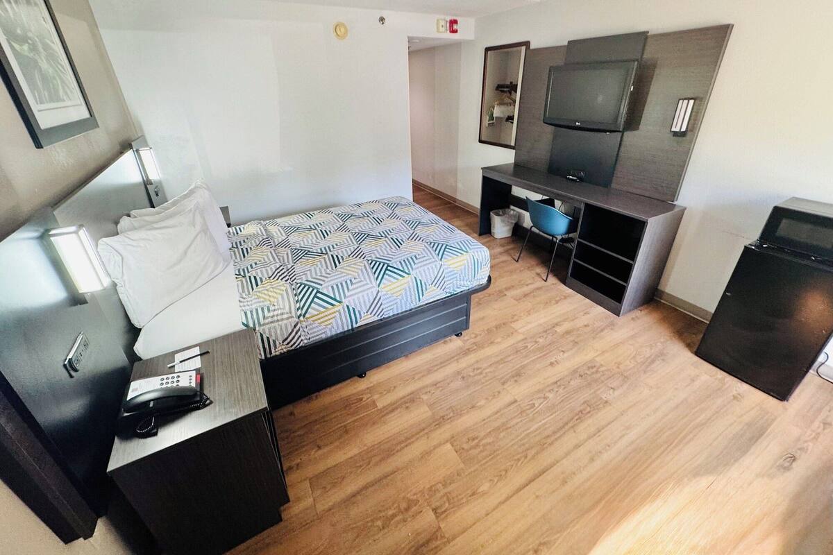 Ein Hotelzimmer mit Bett, Schreibtisch, Stuhl, Fernseher und kleinem Kühlschrank.