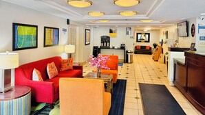 A hotel lobby with a red sofa, orange armchair, and a coffee station.