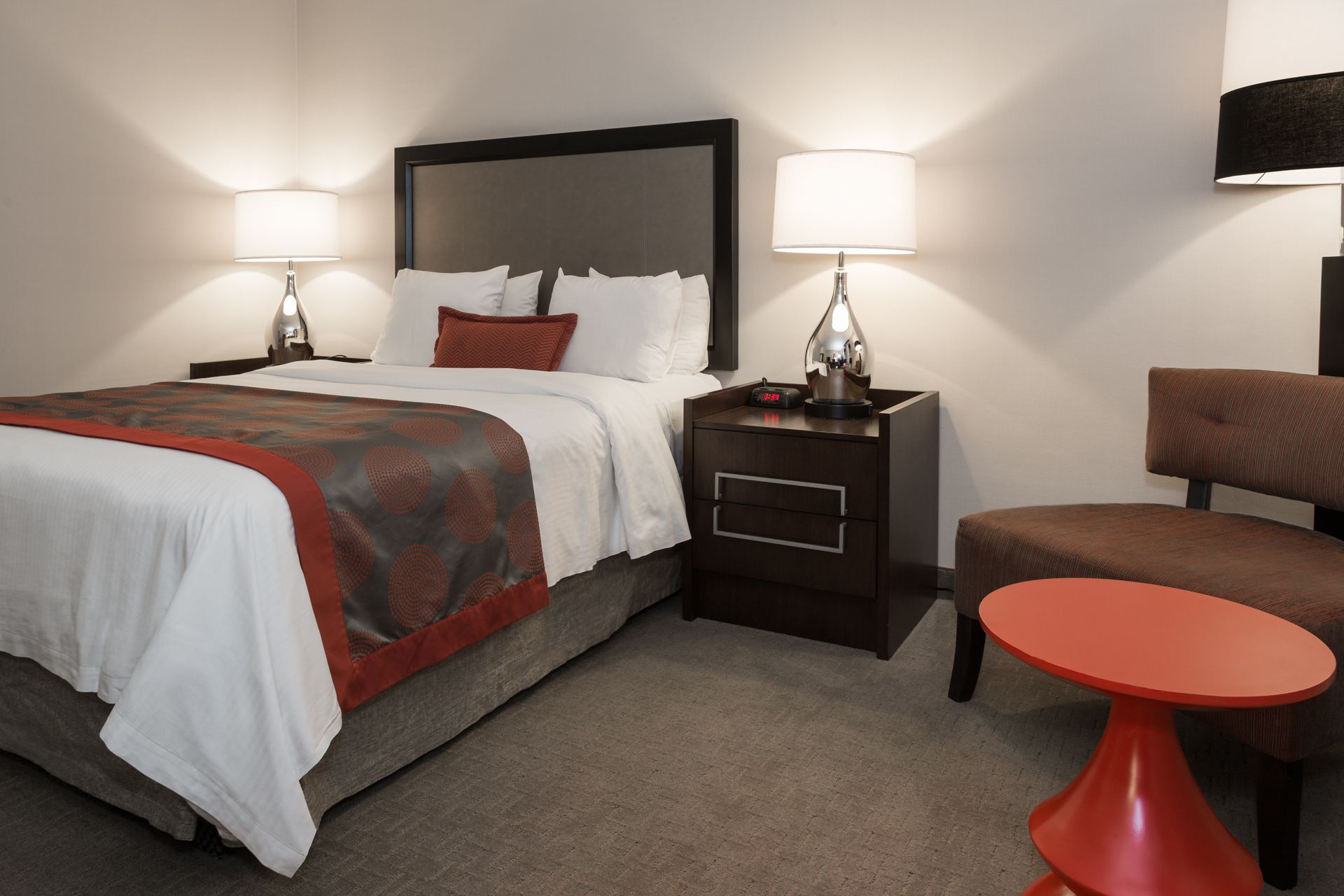 A hotel room with a bed, two bedside tables with lamps, a chair, and a small table.