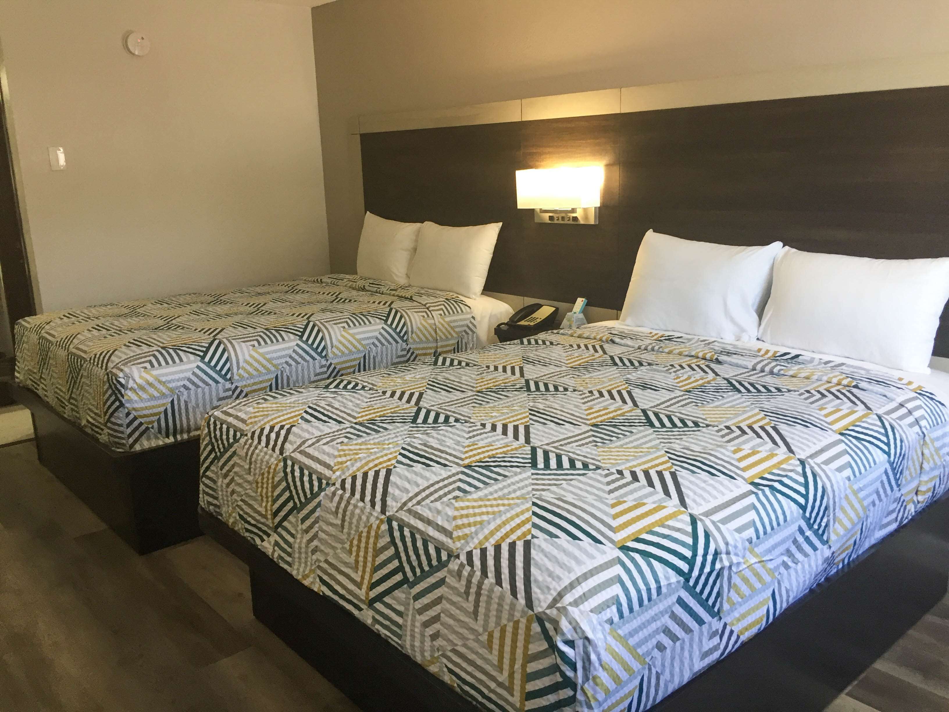 Habitación de hotel con dos camas, cada una con ropa de cama estampada, una mesita de noche con lámpara y teléfono.